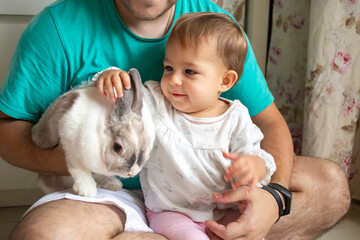 Fototapeta na wymiar adorable baby sits in dad's arms and strokes a decorative rabbit. domestic animals in a family with children. father shows little child easter bunny