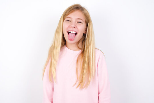 beautiful caucasian little girl wearing pink hoodie over white background with happy and funny face smiling and showing tongue.