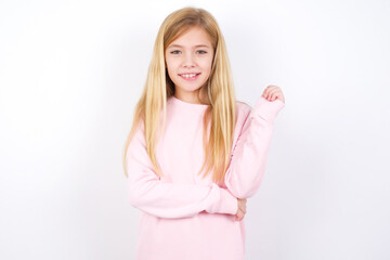 Cheerful beautiful caucasian little girl wearing pink hoodie over white background with hand near face. Looking with glad expression at the camera after listening to good news. Confidence.