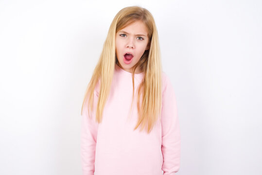 Expressive facial expressions. Shocked stupefied beautiful caucasian little girl wearing pink hoodie over white background, keeps jaw dropped feels stunned from what he sees aside.