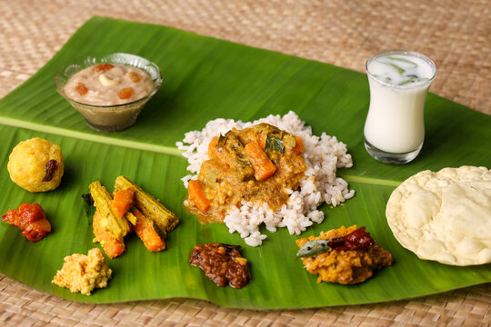 Onam sadhya, Indian women eating with hand boiled rice, served on banana leaf Kerala Indian festival with curries Sambar, Avial, Papadum, Payasam, Banana, Yogurt or Buttermilk
