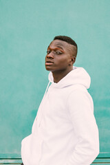 Young african black man against a green wall looking at camera wearing a white sweatshirt with style and confidence