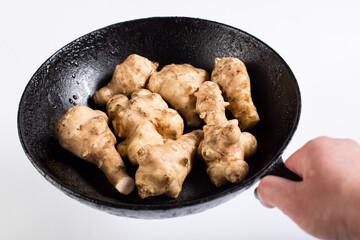 Hand hold pan with jerusalem artichokes. Jerusalem artichokes on frying pan.