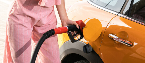 A woman in a suit drives an orange car with gasoline at a gas station in the summer. Hand and red...