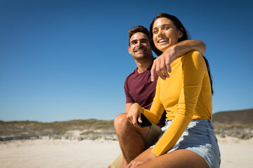 Happy caucasian couple on the beach embracing woman holding smartphone