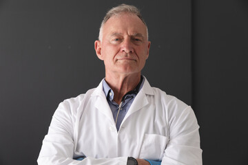 Portrait of caucasian senior male doctor wearing white coat standing with arms crossed, smiling