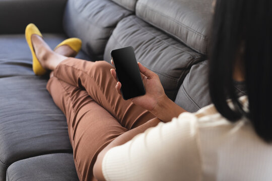 Mixed race gender fluid man relaxing at home on couch using smartphone, with copy space screen