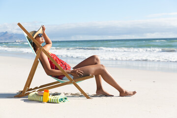 Mixed race woman on beach holiday sitting in deckchair sunbathing