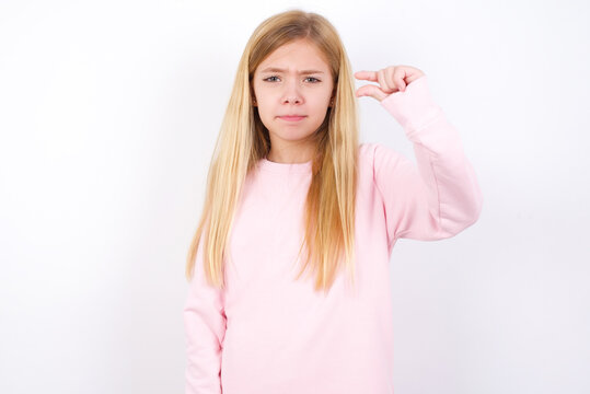 Upset Beautiful Caucasian Little Girl Wearing Pink Hoodie Over White Background Shapes Little Gesture With Hand Demonstrates Something Very Tiny Small Size. Not Very Much