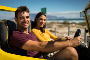 Portraits of happy caucasian couple looking to camera sitting in beach buggy by the sea talking