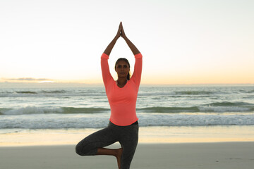 Fototapeta na wymiar Mixed race woman on beach practicing yoga during sunset