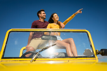 Happy caucasian couple sitting in beach buggy by the sea pointing