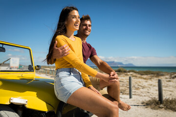 Happy caucasian couple sitting on beach buggy by the sea holding hands