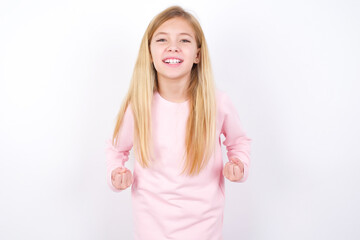 beautiful caucasian little girl wearing pink hoodie over white background raising fists up screaming with joy being happy to achieve goals.