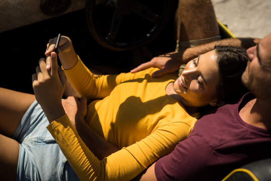 Caucasian couple lying on a beach buggy by the sea using smartphone - Powered by Adobe