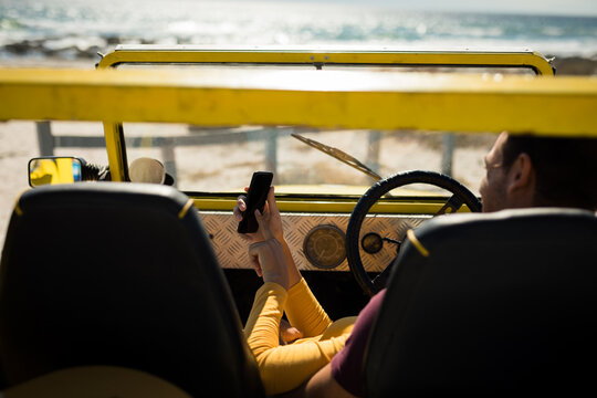 Caucasian couple lying on a beach buggy by the sea using smartphone