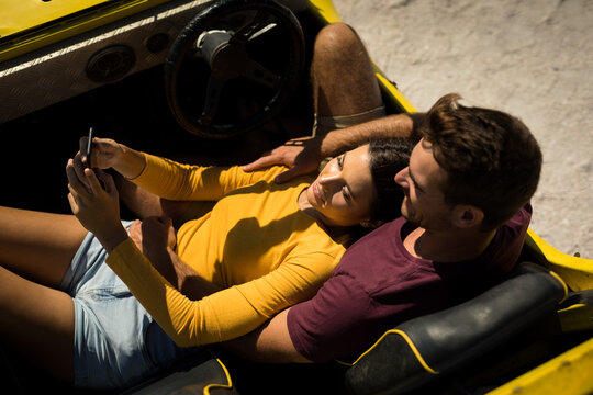 Caucasian couple on a beach buggy by the sea using smartphone - Powered by Adobe