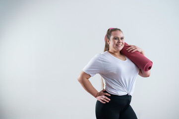 Young fat caucasian woman holding a sport mat. Charming plus size model in sportswear stands on a...