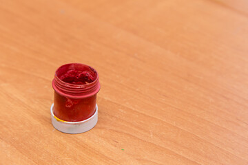 An old open jar of red gouache for painting. Side view of a half-empty can of gouache paint. There...