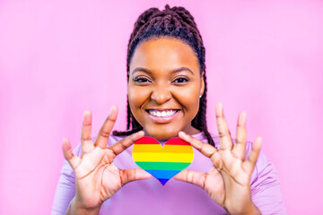 Portrait of an attractive hispanic woman holding a LGBT rainbow heart in pink studio