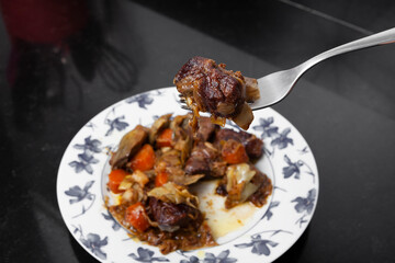 fork with a portion of Beef Ragout with vegetables on a dark background kitchen and selective blur