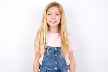 beautiful Caucasian little girl wearing denim overalls over white background with nice beaming...