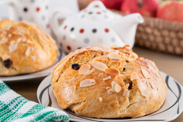 Freshly baked, homemade sweet cake with almonds and raisins on wooden table. Easter loaf. Basket with pears and apples. Tea pot and tea cup with color dots.