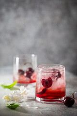 Cold cherry lemonade drink with fresh cherry and ice on gray background