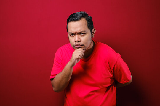 Portrait Of Young Asian Man Staring At Camera With Suspicious Cynical Expression, Arms Crossed On Chest