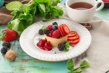 Sweet tart with fresh raspberry strawberry blackberry and cup of tea on the table