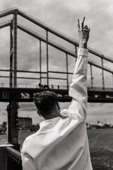 The guy with the raised hand shows the pis gesture on the background of the bridge. Black and white photo.