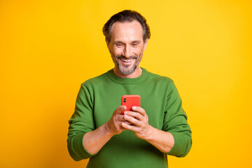 Photo of cheerful man hold telephone look screen wear green pullover isolated bright yellow color background