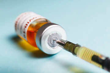 Macro shot of antiviral vaccine vial with syringe for immunization against covid-19 virus. Isolated on blue background with copy space for text. Close up, top view