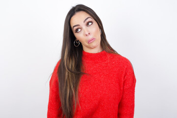 young beautiful brunette woman wearing red knitted sweater over white with snobbish expression curving lips and raising eyebrows, looking with doubtful and skeptical expression, suspect and doubt.