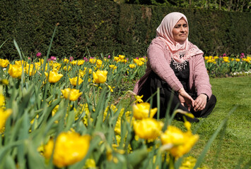 Naklejka na ściany i meble Muslim mature woman sitting relaxed on the grass with flowers in a beuatiful spring day in a Park of London.