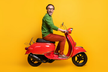 Fototapeta na wymiar Photo of excited man ride scooter open mouth wear glasses green sweater pants shoes isolated yellow color background