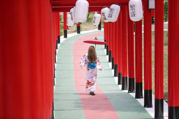 woman in kimono holding umbrella walking into at the shrine red gate, in Japanese garden.