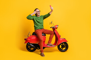Fototapeta na wymiar Photo of guy hold smartphone ride moped take selfie wear specs green sweater pants shoes isolated yellow color background
