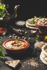 Classic hummus in a bowl with ingredients on dark background. Vertical format.