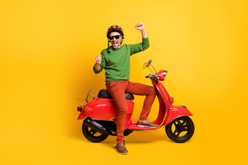Fototapeta na wymiar Photo of excited man on bike raise fists wear helmet specs green pullover pants shoes isolated yellow color background