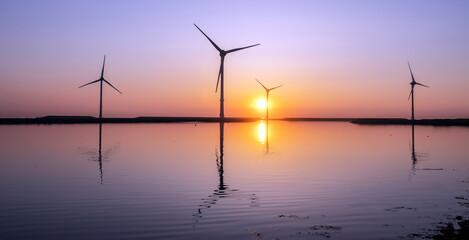 wind turbines and colorful sunrise reflected in water