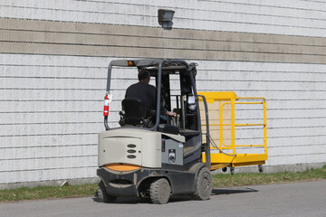 Guy driving a forklift outside a factory in the parking lot with a fire extinguisher attached to one of the posts

