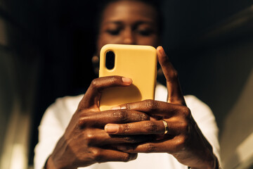 view from below of an afro or black girl's hands with a cell phone. American woman communicating with her smartphone. Hands of young black girl holding a phone. - obrazy, fototapety, plakaty