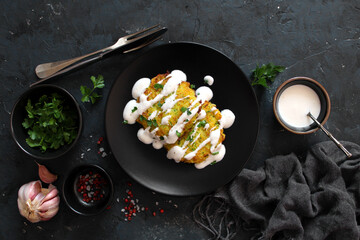 Potato pancakes with zucchini served with sour cream on dark table. Top view with copy space.