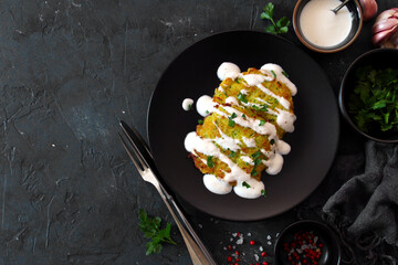 Potato pancakes with zucchini served with sour cream on dark table. Top view with copy space.