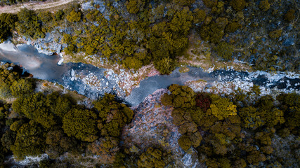 vista área cenital de un arroyo abriéndose camino entre las piedras en una tarde otoñal, con sus aguas cristalinas reflejando las nubes del cielo.