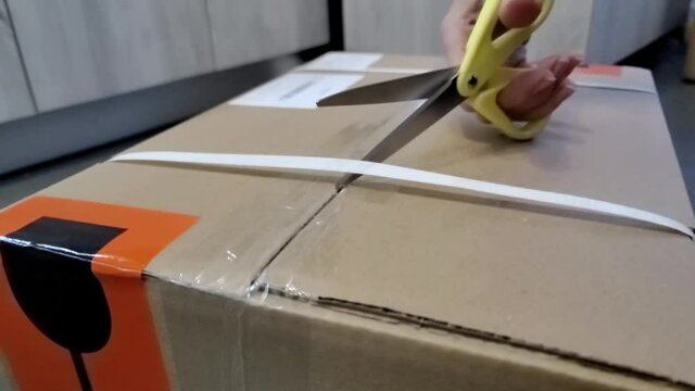 Cutting brown tape with scissors and sealing a cardboard box