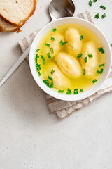 Griessnockerlsuppe. Soup with semolina dumplings in a white bowl on a light concrete background top view. Bavarian cuisine. Free space for text