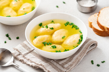 Griessnockerlsuppe. Soup with semolina dumplings in a white bowl on a light concrete background. Bavarian cuisine.