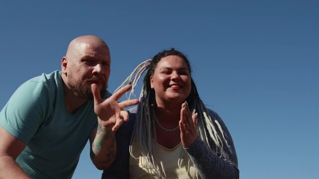 Body positive fat friends enjoy life and sunny weather. Two young happy people dance on background of bright blue sky. Music and copy space concept. man with tattoo and a woman with dreads dancing.